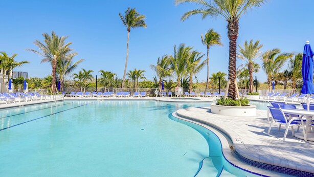 A swimming pool with blue lounge chairs and palm trees. - Sunny Ocean Village Beach Condo: Community Pool (Fort Pierce)