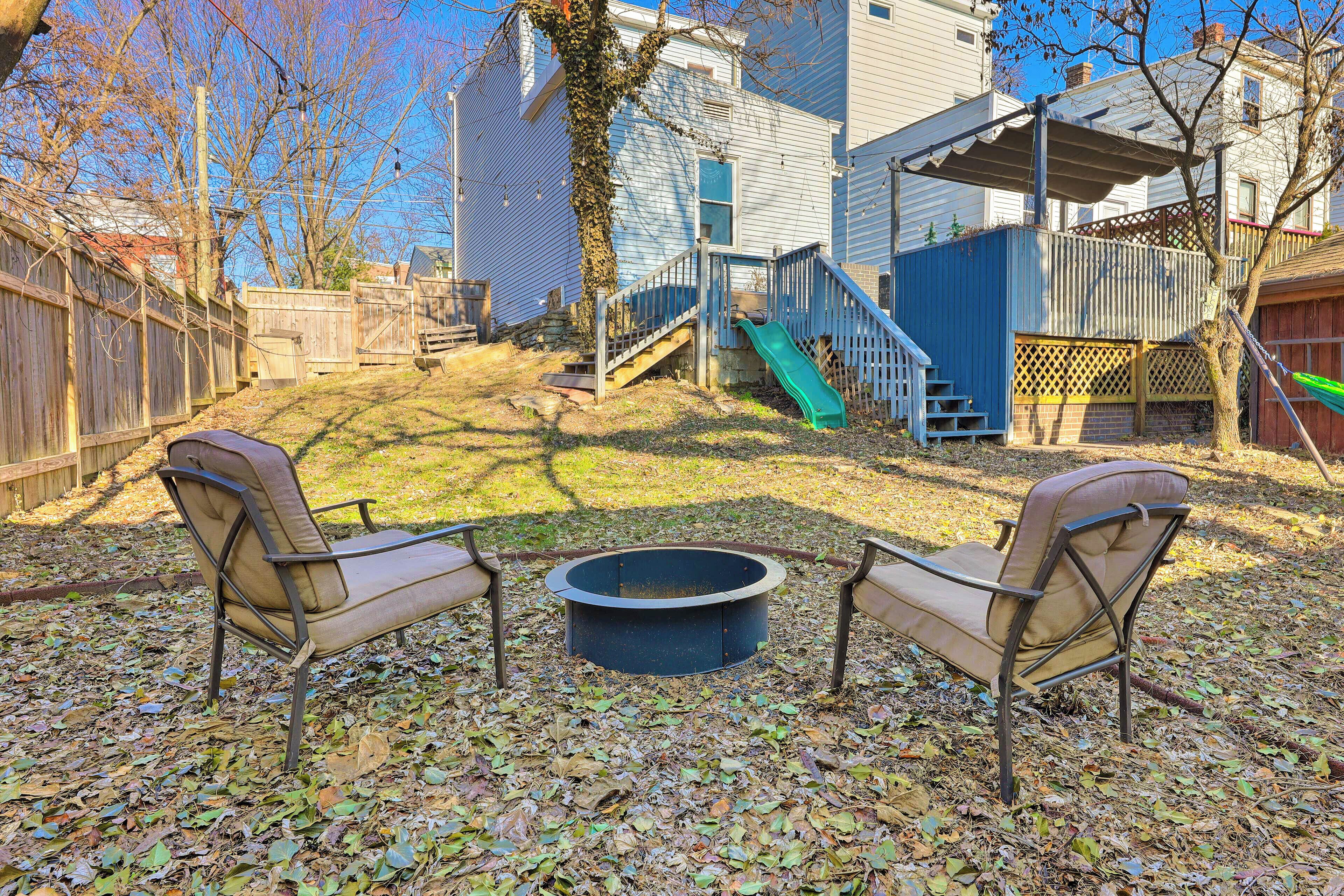 A backyard with a fire pit, two chairs, a slide, and a wooden fence.