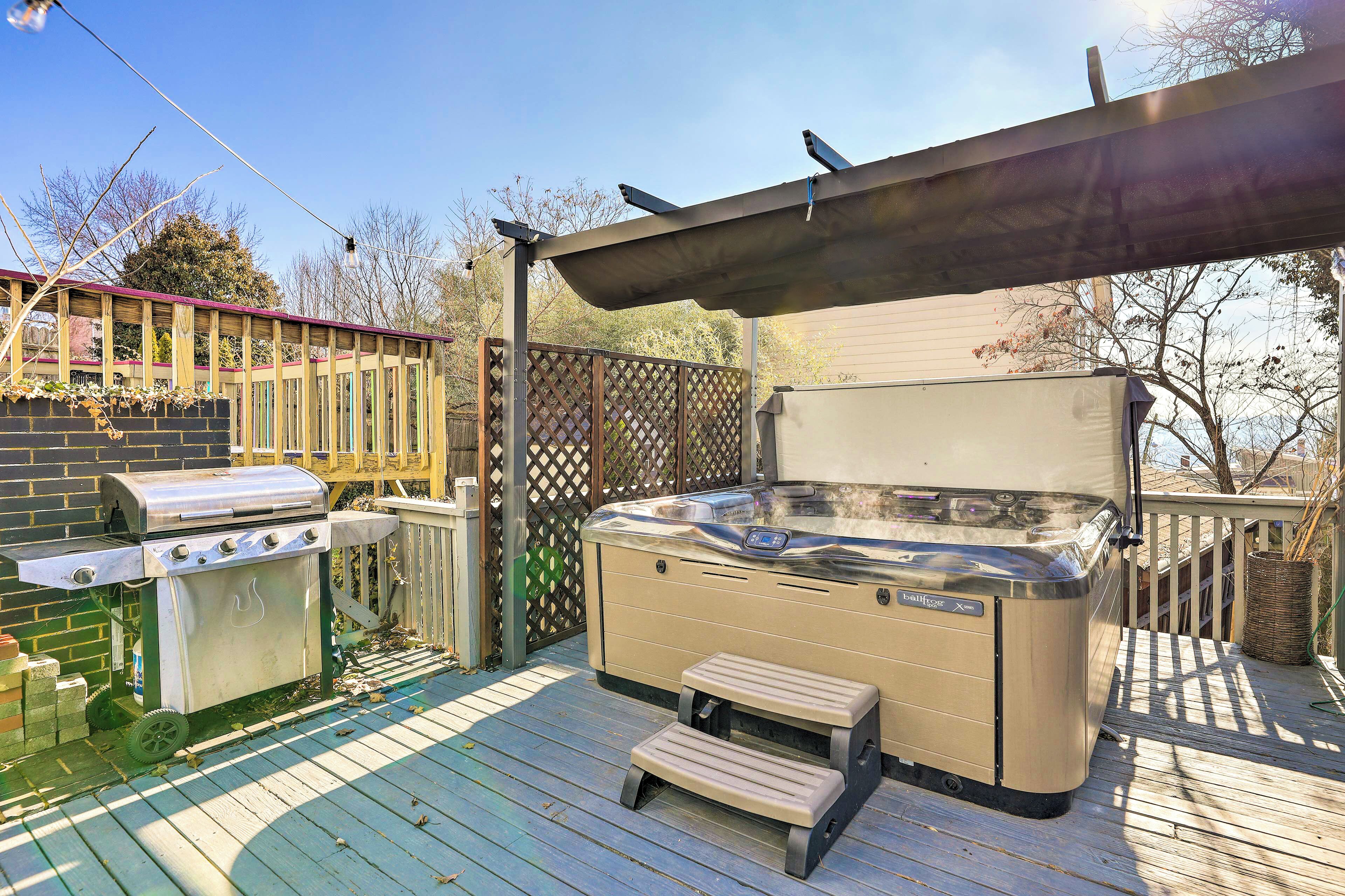 A backyard with a hot tub, a grill, and a wooden deck.