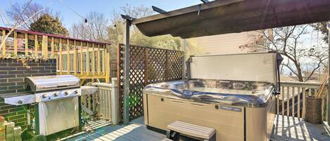 A backyard with a hot tub, a grill, and a wooden deck.