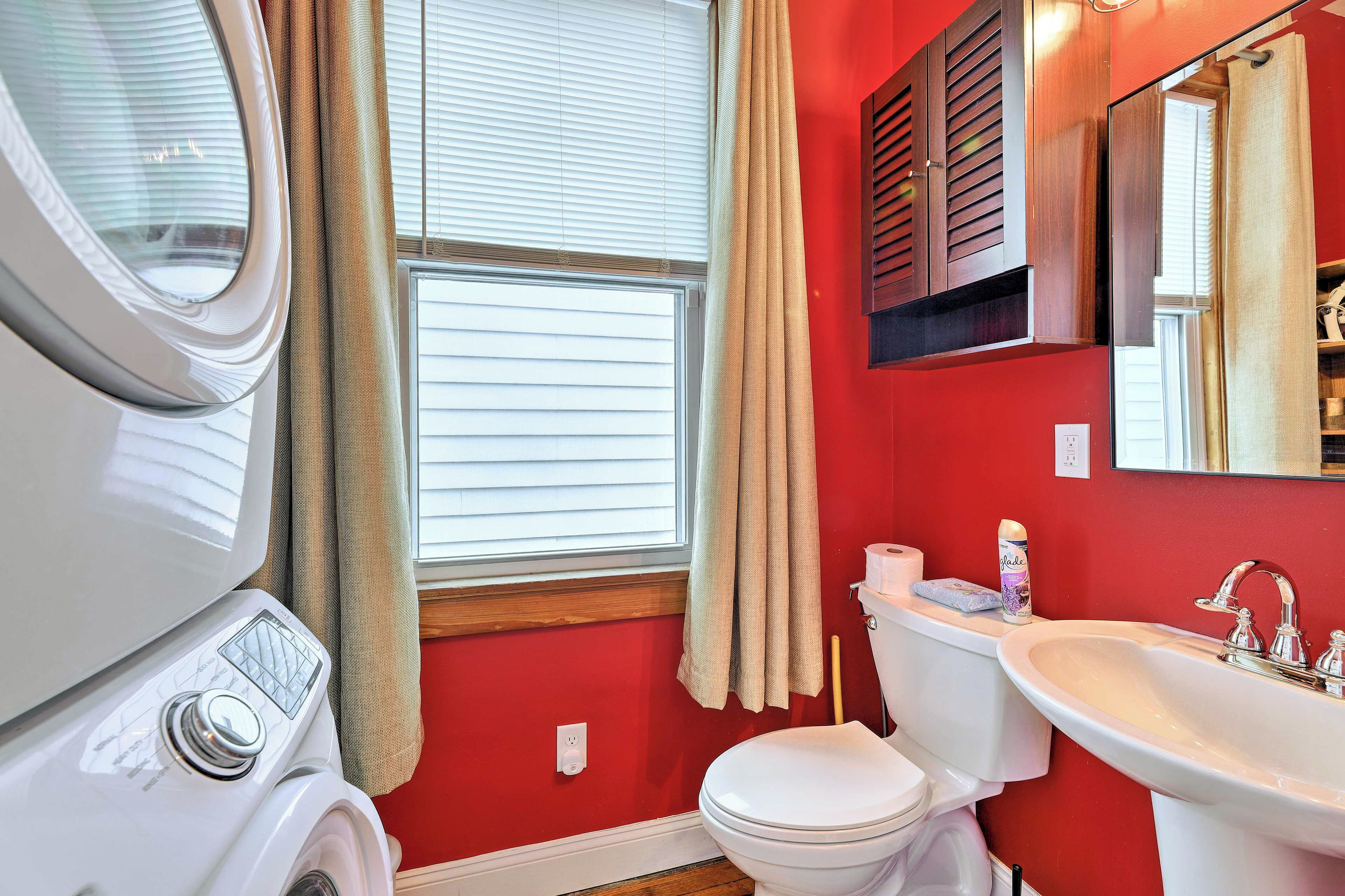 A bathroom with a red wall, a white toilet, a white sink, and a window with blinds.