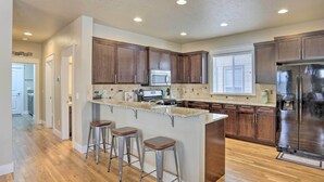 A modern kitchen with wooden cabinets, a stainless steel refrigerator, a built-in island with stools, and a window providing natural light. - Charming Boise Home ~ 8 Mi to Downtown! (Garden City)