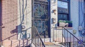 A building entrance with a metal gate, a brick wall, a window with a planter, and a staircase with a metal railing. - Cincinnati Retreat w/ Patio & Grill! (Cincinnati)