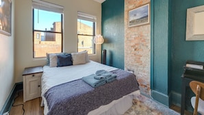A bedroom with a bed, two windows, a nightstand, a lamp, and a brick wall. - Cincinnati Retreat w/ Patio & Grill! (Cincinnati)