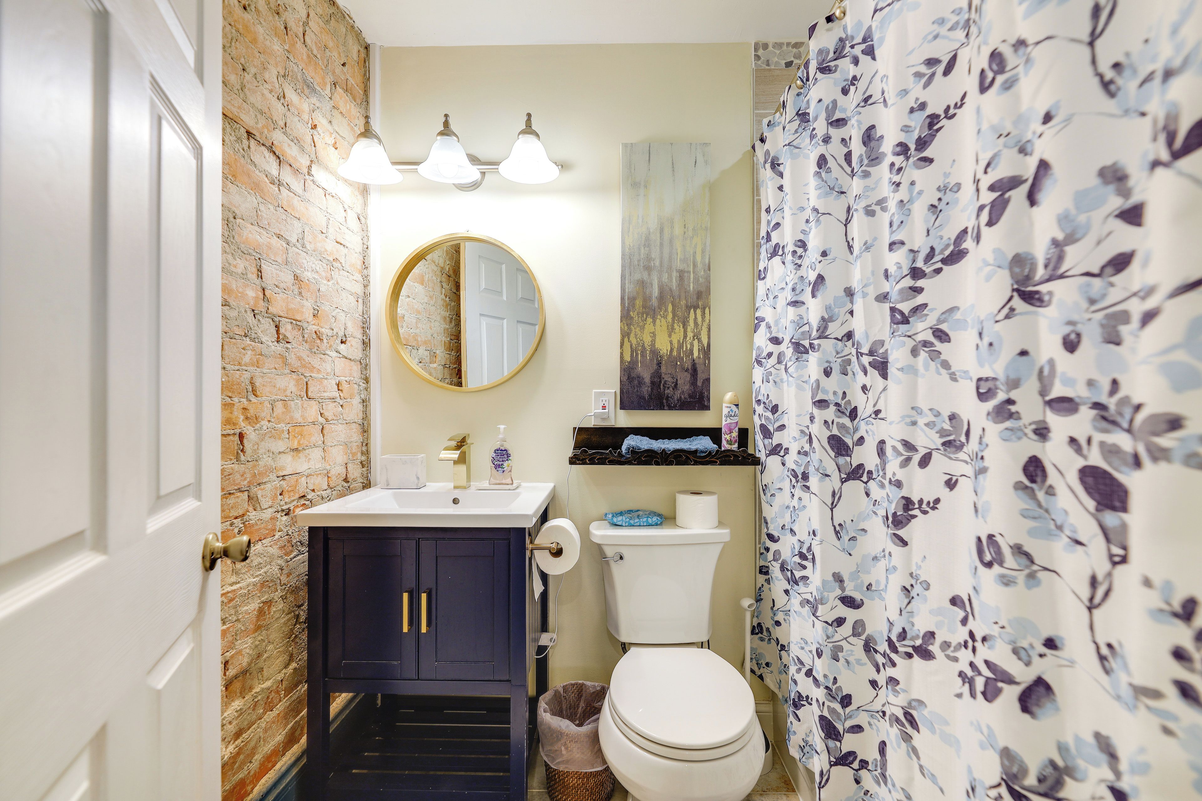 Un baño con pared de ladrillo, un espejo redondo, un inodoro y un lavamanos con una toalla azul.