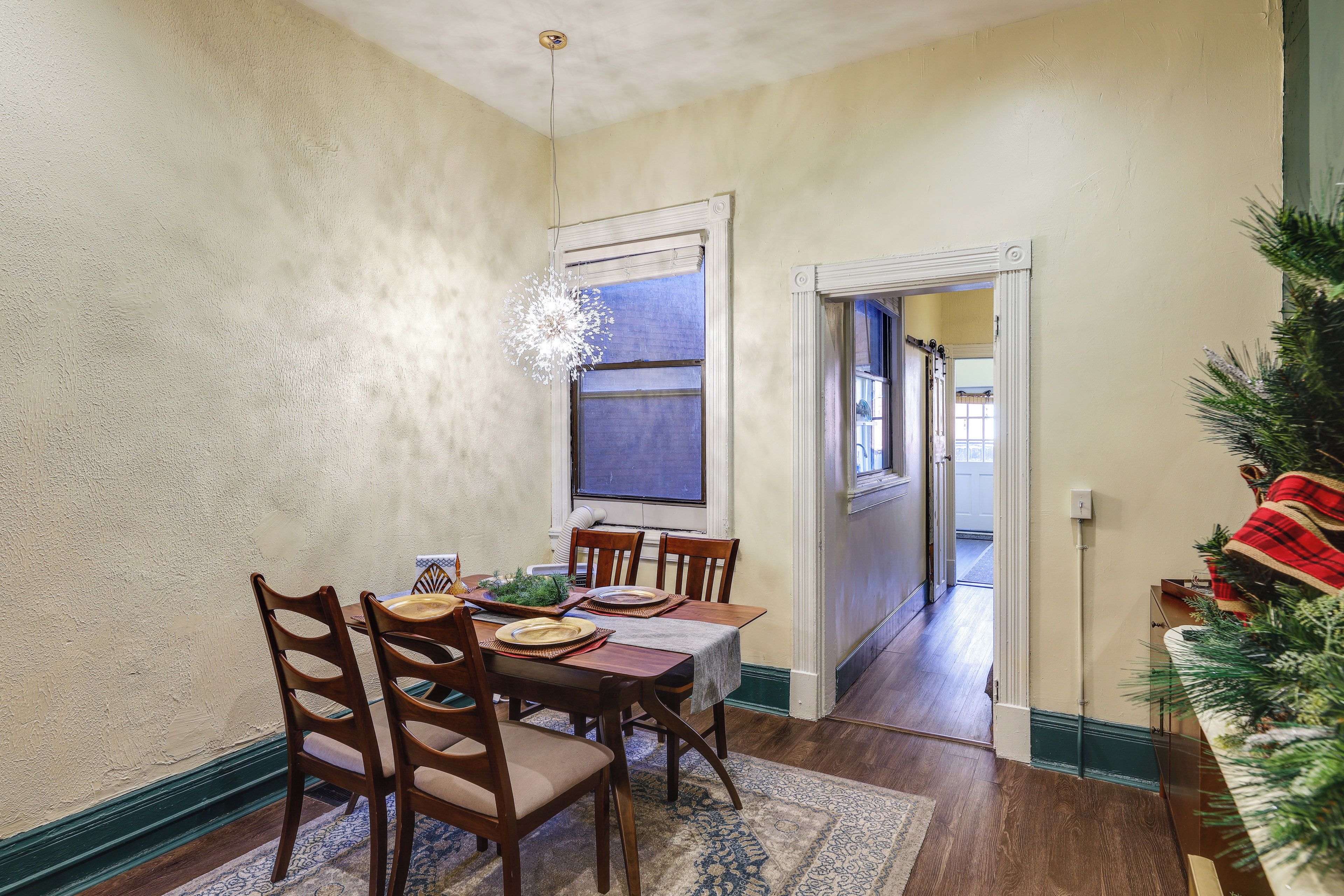 A dining area with a table set for four, wooden chairs, a chandelier, and a Christmas tree.