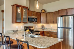 A kitchen with granite countertops, stainless steel appliances, wooden cabinets, and pendant lighting. - Lake Chelan 'manson Bay' Condo w/ Pool Access! (Manson)