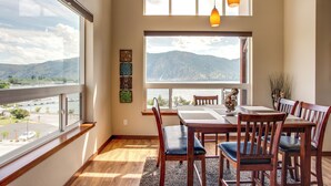 A dining area with a table and chairs, large windows with a view of mountains, and a hanging pendant light. - Lake Chelan 'manson Bay' Condo w/ Pool Access! (Manson)