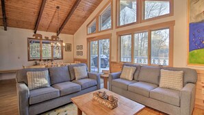 Ein gemütliches Wohnzimmer mit zwei grauen Sofas, einem Holztisch und großen Fenstern mit Blick ins Freie.