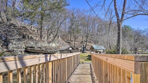 A wooden boardwalk leading through a wooded area with a rocky hillside and a small building with a green roof. - Peaceful Cookeville Cabin in Unique Setting (Cookeville)