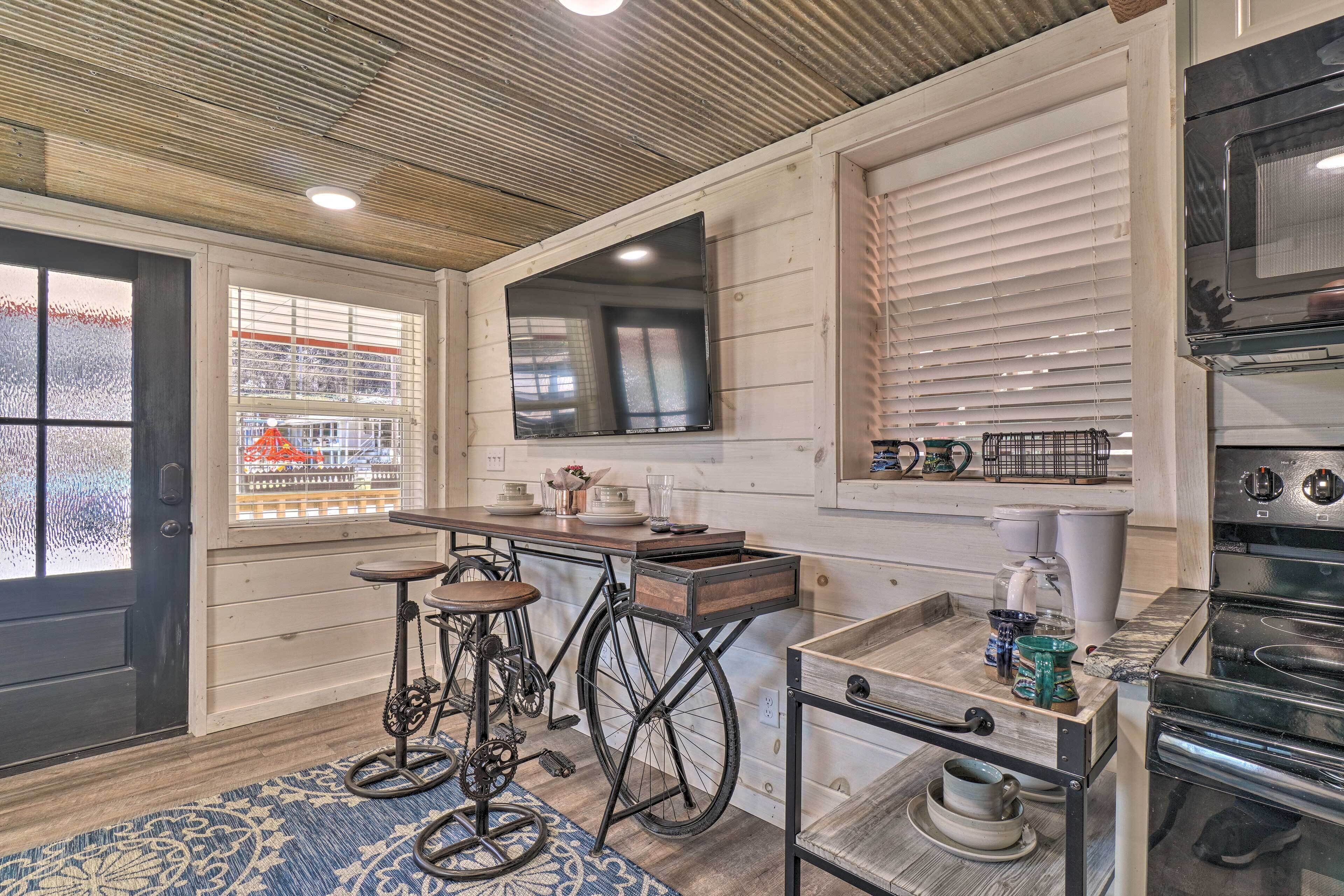 A kitchen with a wooden ceiling, a window with blinds, a stove, and a bar stool.