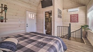 A cabin interior with a checkered bed, a mounted television, a shower area, and a sign listing cabin rules. - Peaceful Cookeville Cabin in Unique Setting (Cookeville)