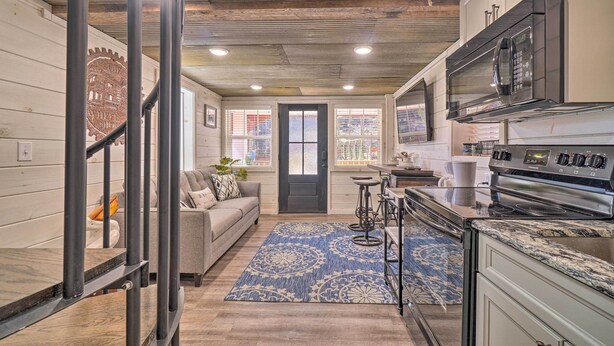 A modern kitchen with a built-in microwave, oven, and stainless steel appliances. There is a wooden staircase leading to another level, and a blue patterned rug on the floor. - Peaceful Cookeville Cabin in Unique Setting (Cookeville)