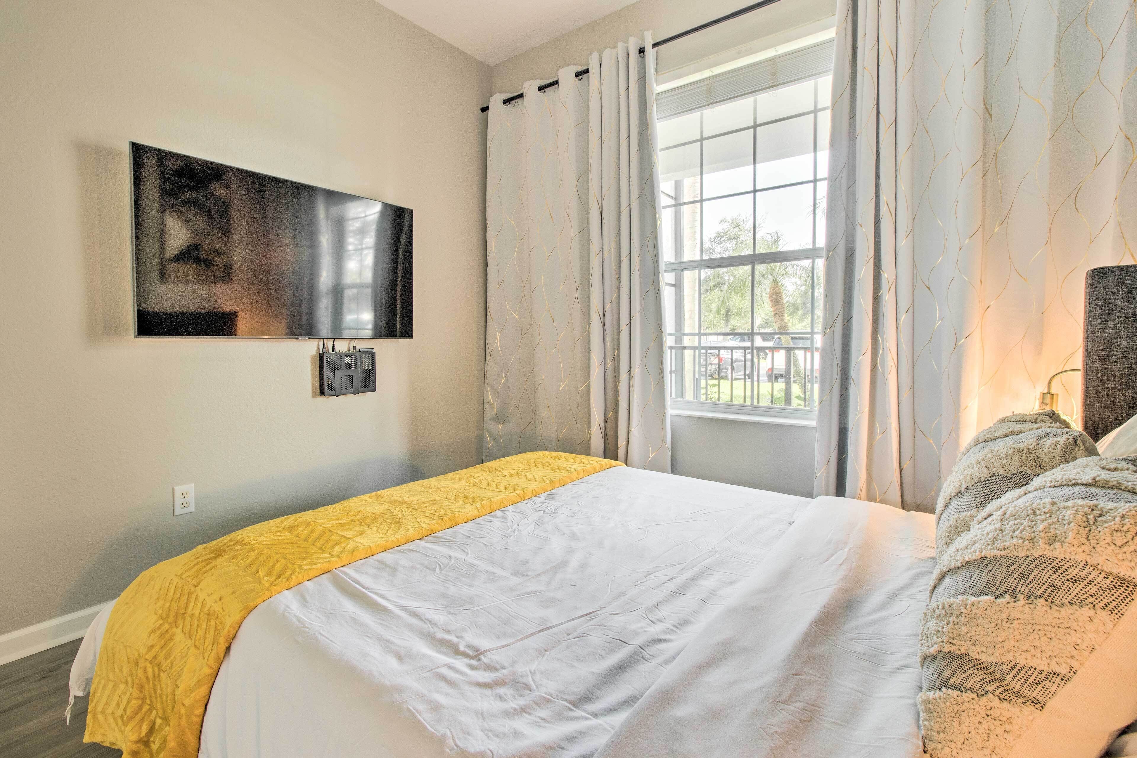 Ein Schlafzimmer mit einem Bett, einem an der Wand montierten Fernseher und einem Fenster mit Vorhängen.