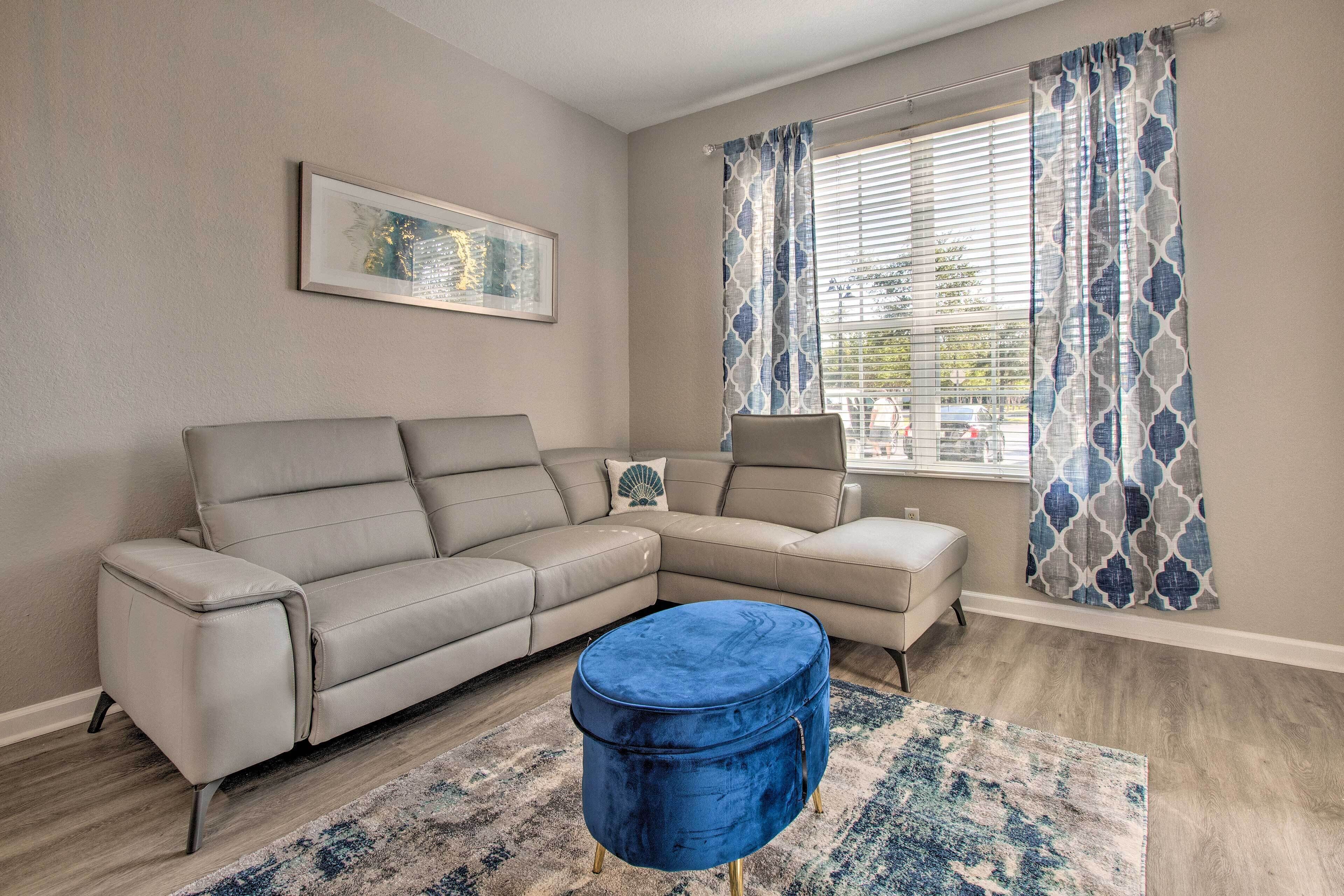 A living room with a beige sectional sofa, a blue ottoman, and a patterned rug.