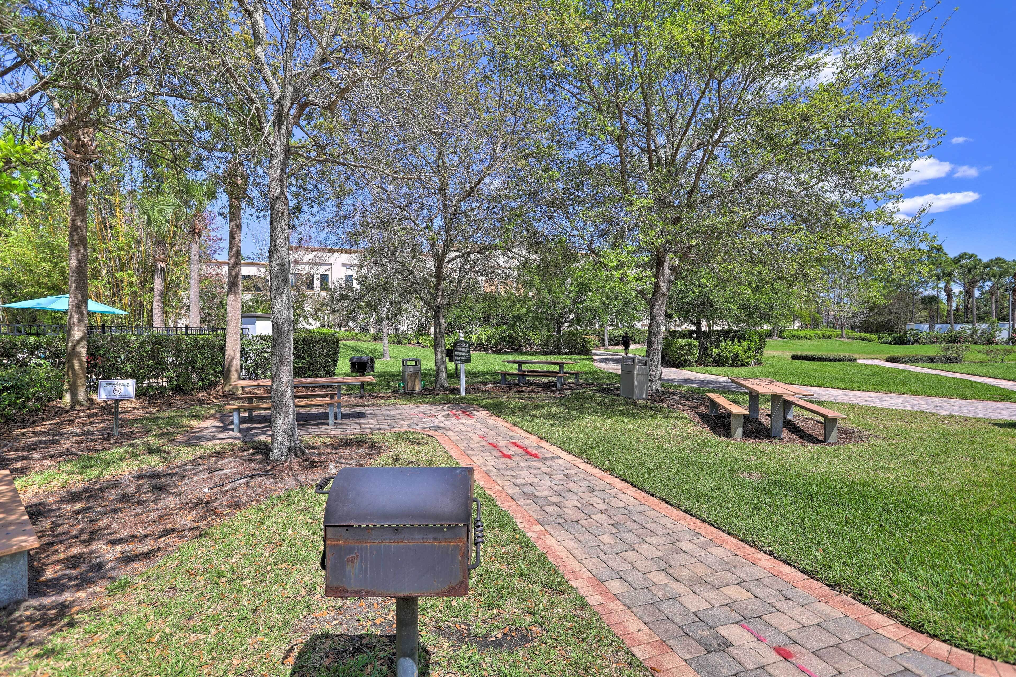 A park with a paved walkway, benches, and trees.