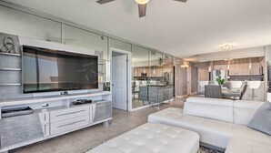 A modern living room with a large flat-screen TV, white sofas, and a glass partition separating it from the kitchen area. - The Terrace at Pelican Beach Resort: View + Pool! (Destin)