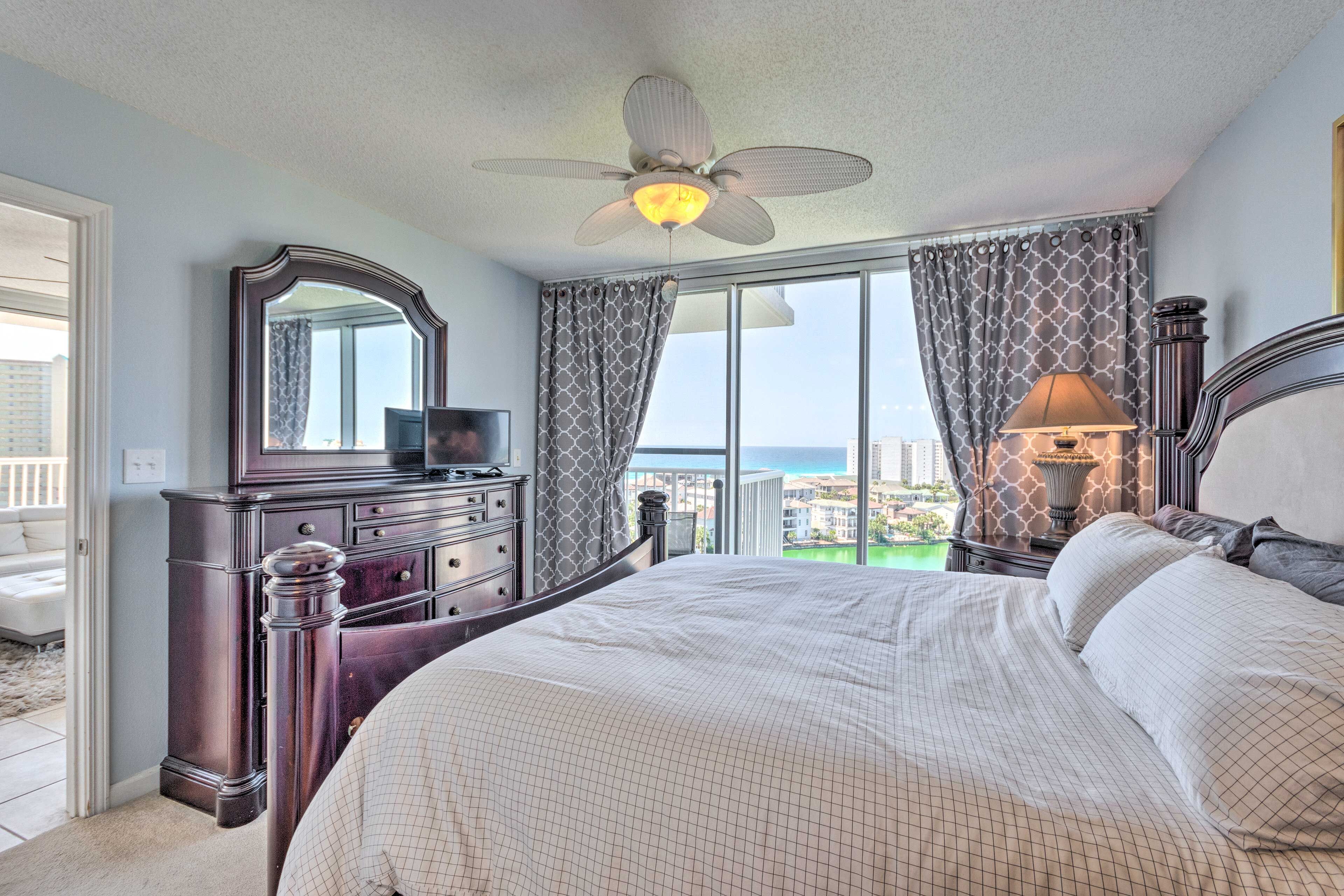 Een slaapkamer met een groot bed, een dressoir, een spiegel, een plafondventilator en uitzicht op de oceaan.