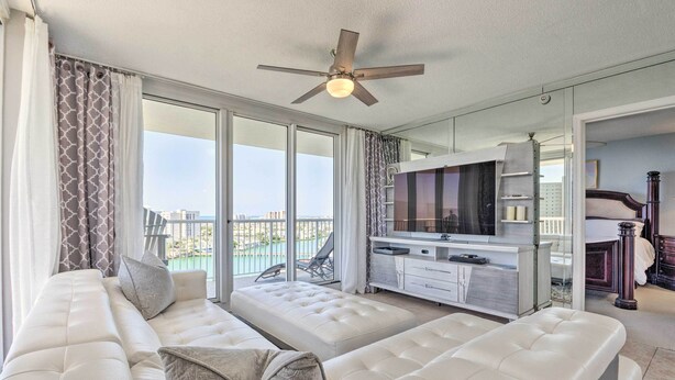 A modern living room with a large sofa, a TV, and a balcony with a view. - The Terrace at Pelican Beach Resort: View + Pool! (Destin)