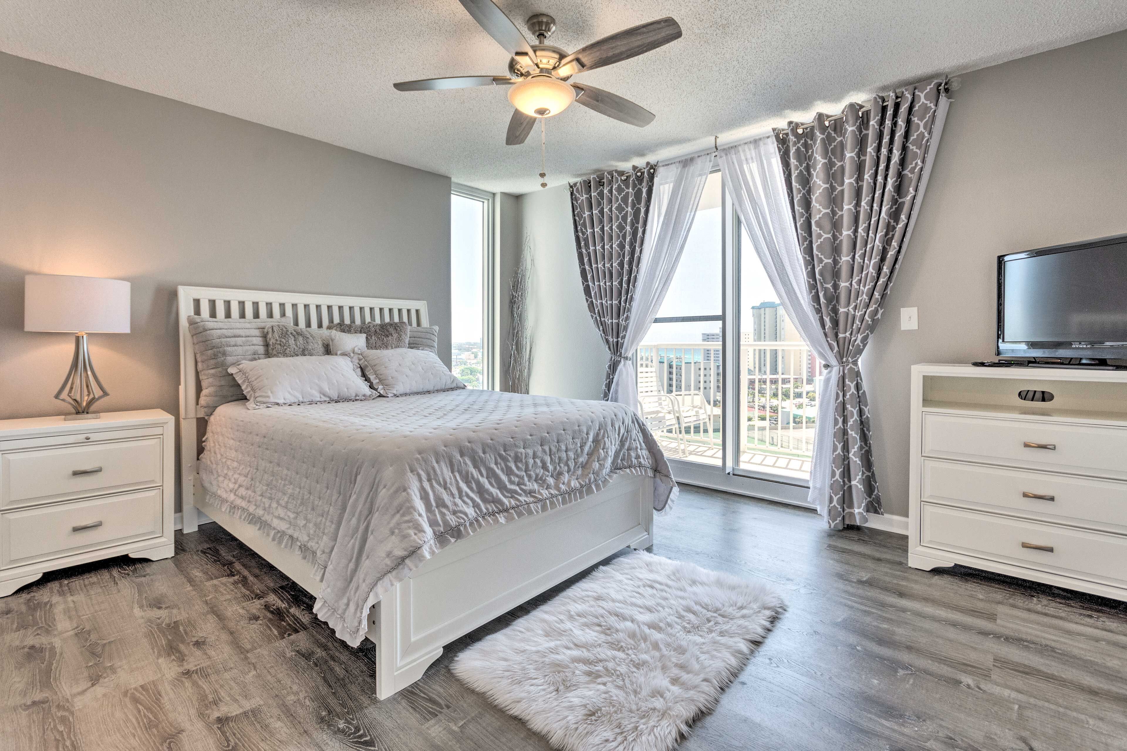 Une chambre à coucher comprenant un lit, une table de chevet, une commode, un téléviseur et un ventilateur de plafond.