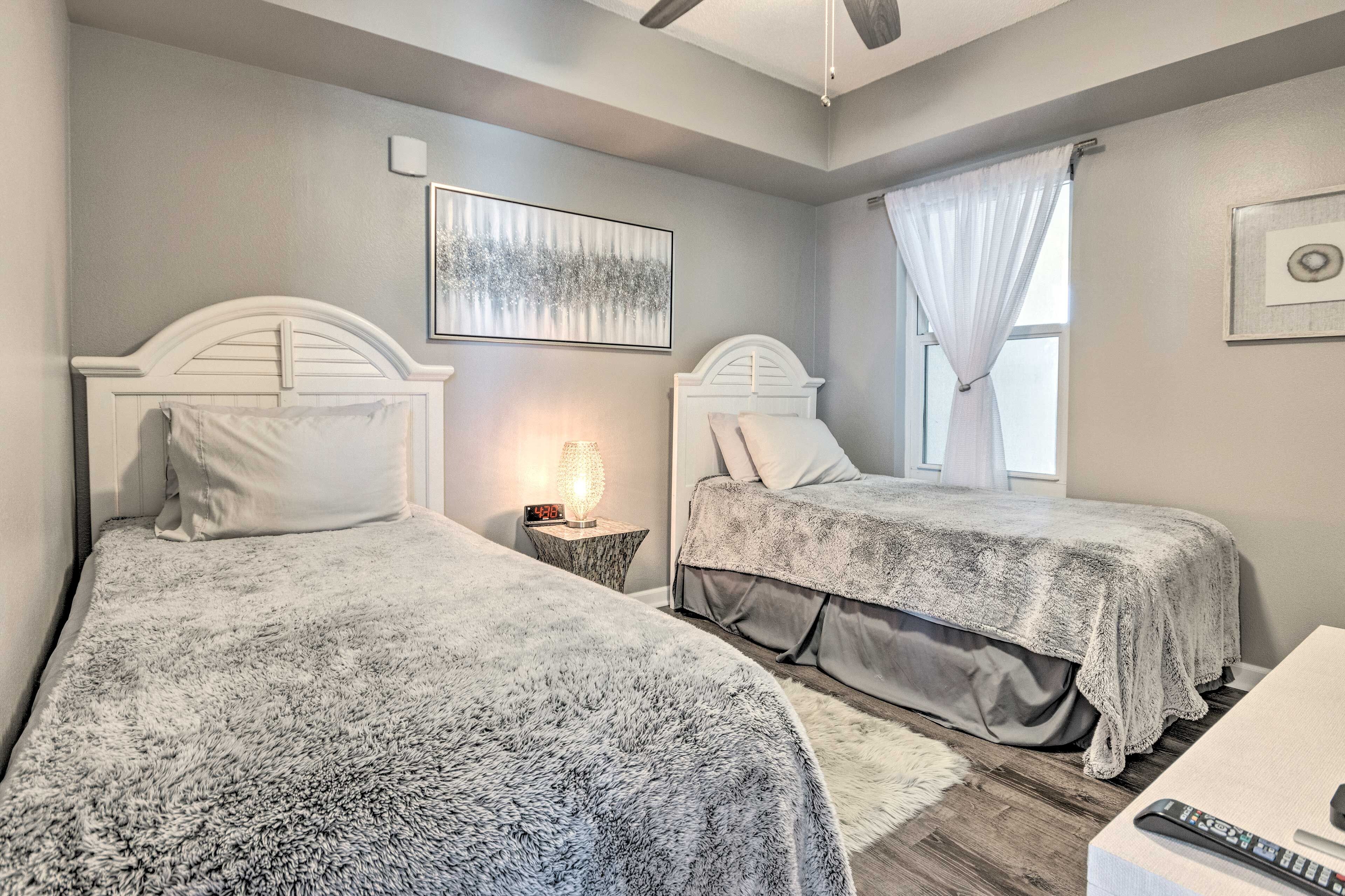 A bedroom with two beds, a nightstand with a lamp, a framed picture on the wall, and a window with curtains.
