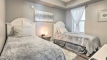 A bedroom with two beds, a nightstand with a lamp, a framed picture on the wall, and a window with curtains.