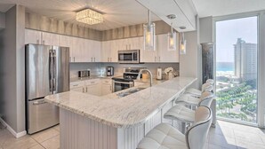 A modern kitchen with a large island, stainless steel appliances, and a view of a coastal cityscape. - The Terrace at Pelican Beach Resort: View + Pool! (Destin)