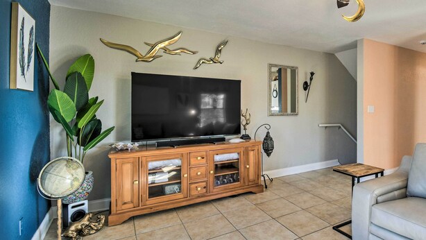 A living room with a large flat-screen TV, wooden entertainment unit, and a grey sofa. - 'breezy Heights' Townhome < 1 Mi to Beach (Pensacola)