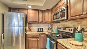 Una cocina con armarios de madera, electrodomésticos de acero inoxidable, encimeras de granito y un recipiente para utensilios de color verde azulado.