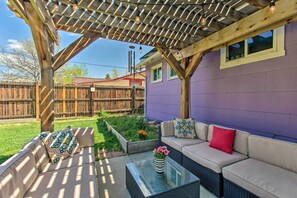 A covered patio with a wooden pergola, a beige sofa, a glass coffee table, and a flower vase. - Patio, Grill & Yard: Cozy Denver Abode! (Denver)