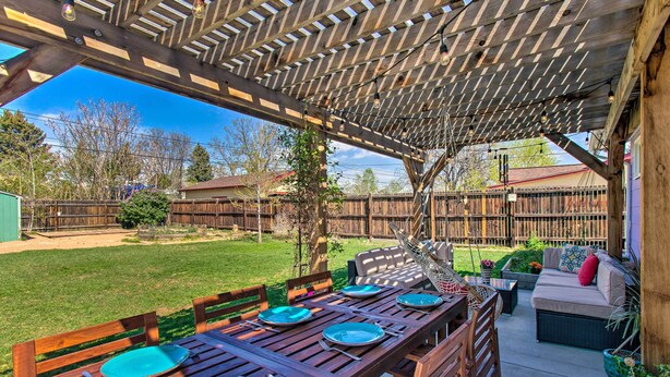Un patio exterior con una mesa de madera dispuesta para comer, rodeado de sillas y un área de estar con cojines.