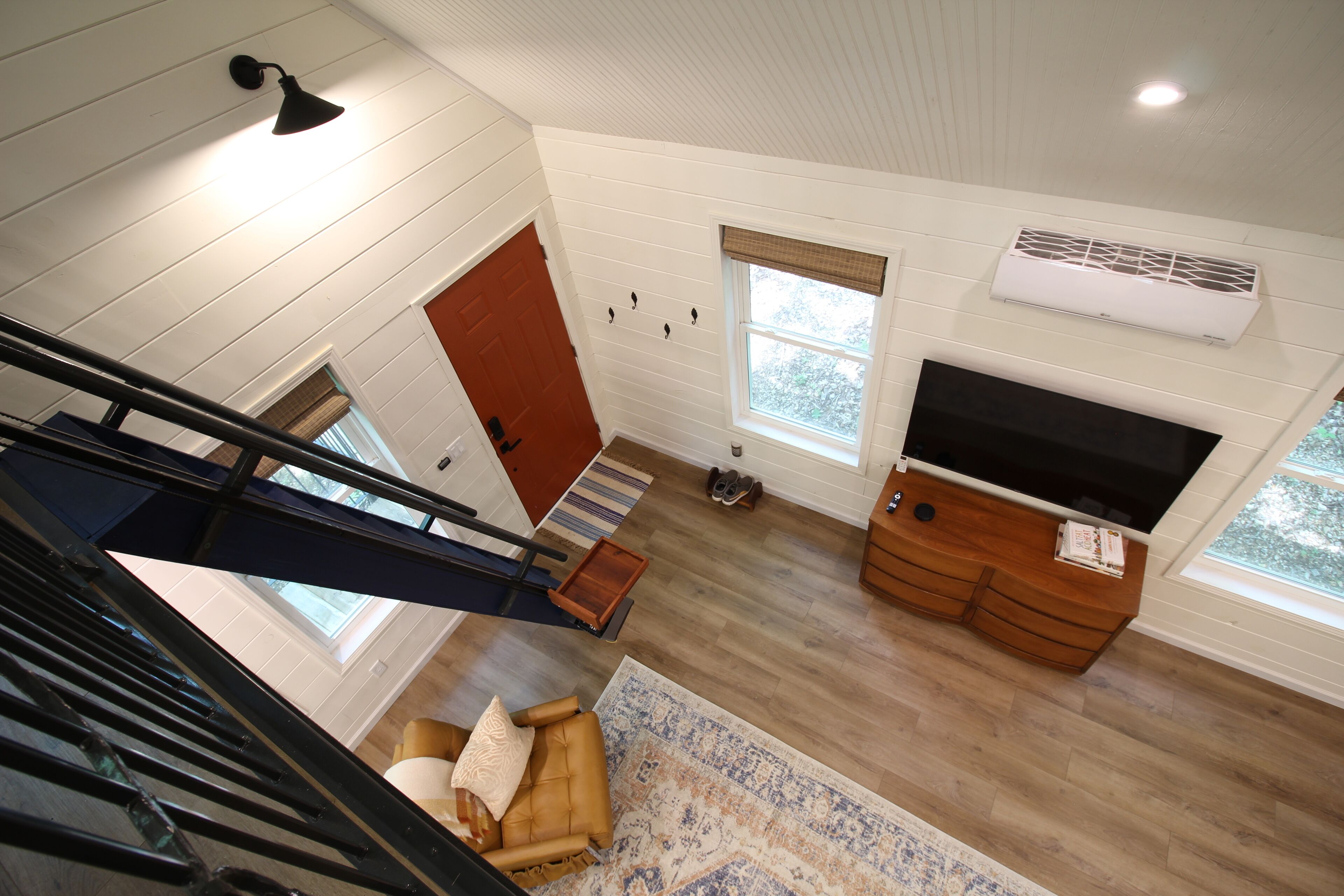 A spacious living area with a high ceiling, a staircase, a fireplace, and a large window.