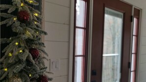 Un árbol de Navidad con luces y adornos junto a una puerta con ventanas.