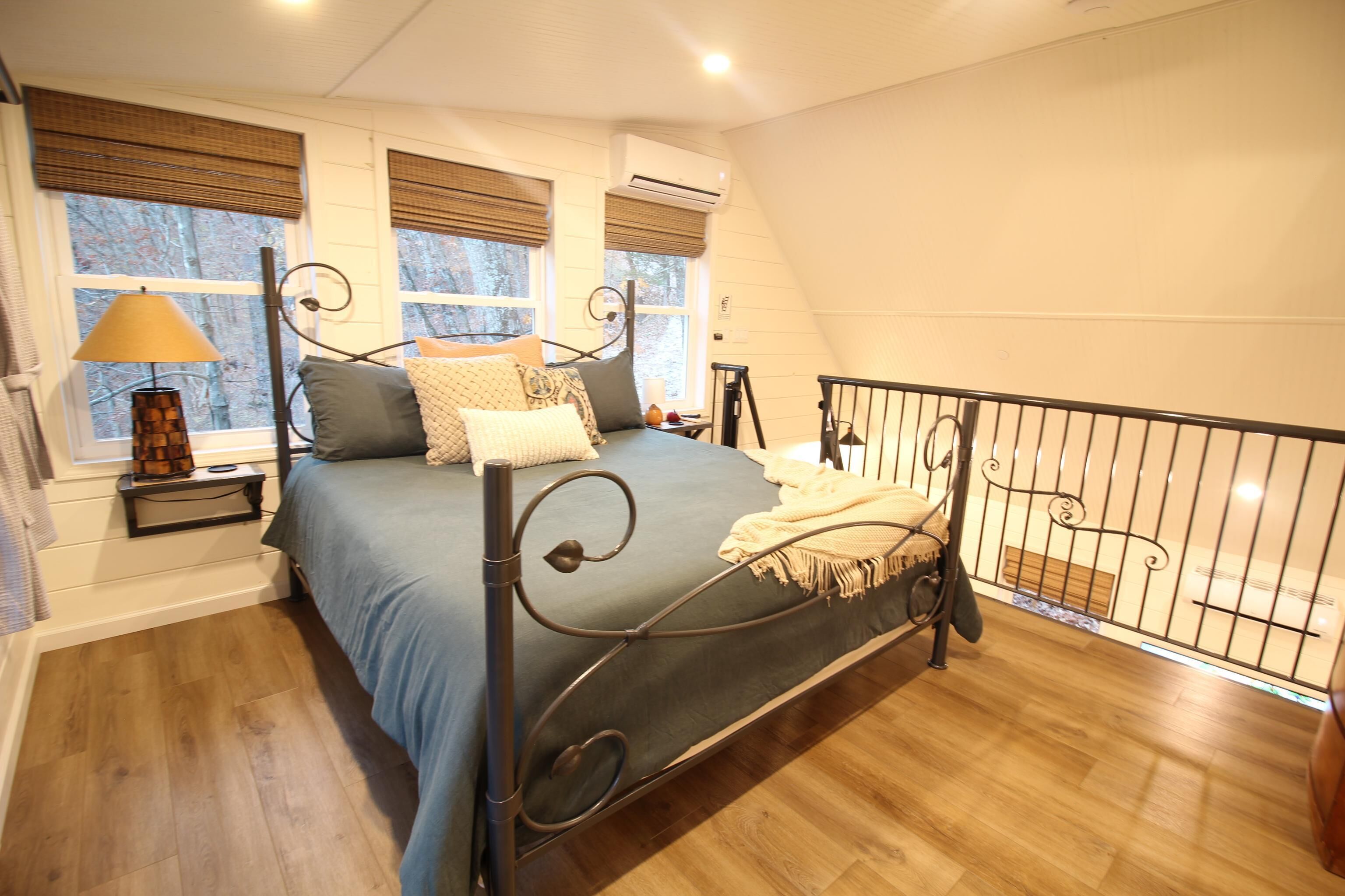 Quarto com cama, mesa de cabeceira, luminária e janela com persianas.