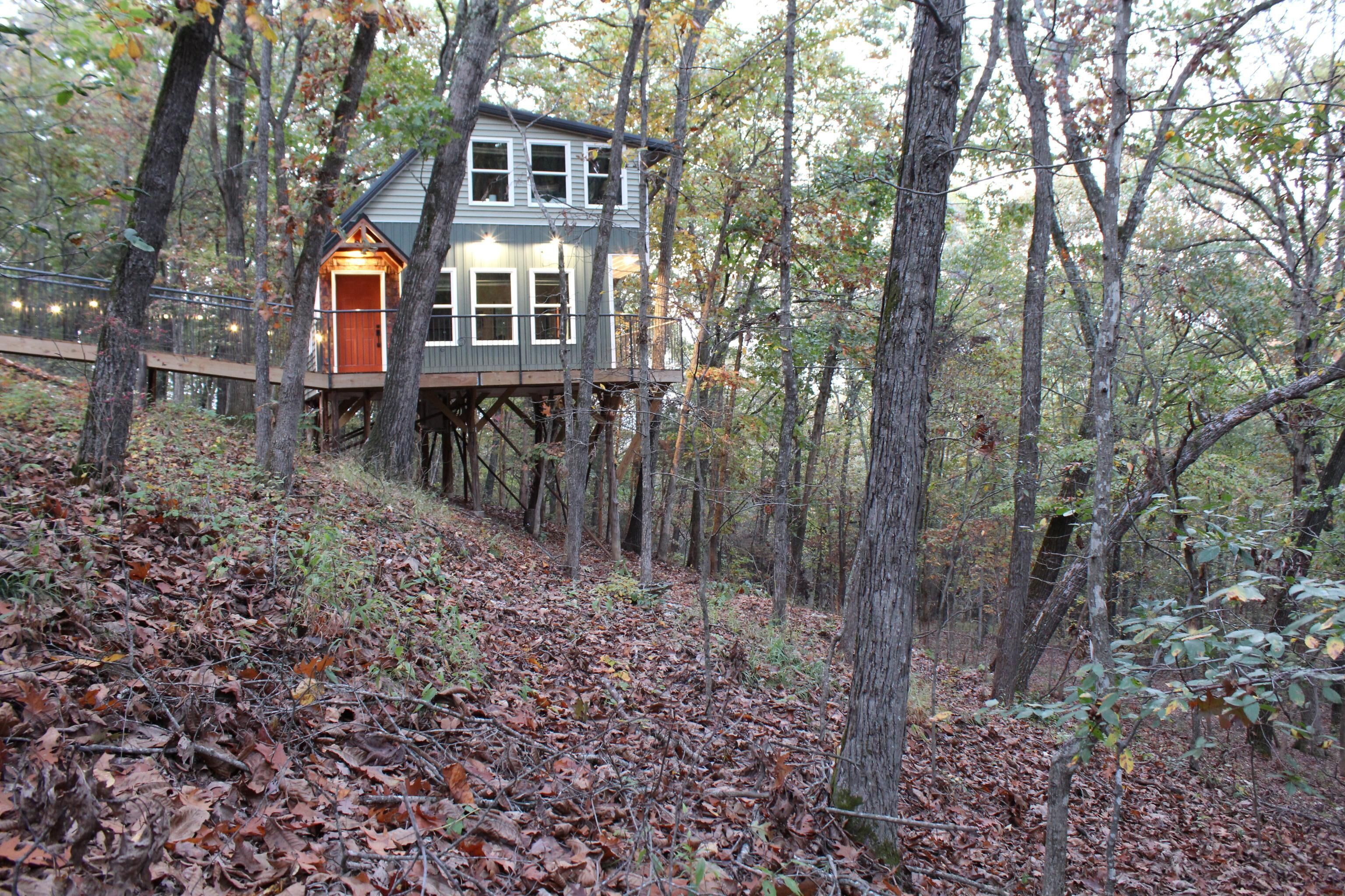 Eine Holzhütte mit einer Holzterrasse und einer Treppe, umgeben von Bäumen und einem mit Blättern bedeckten Waldboden.