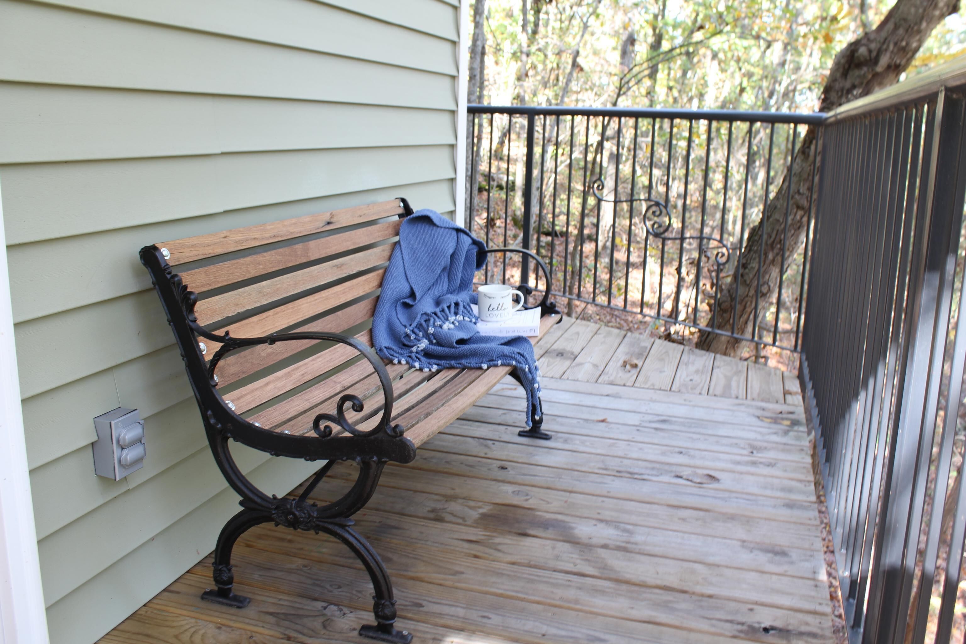 A wooden bench on a wooden deck with a metal railing, a white mug, and a blue cloth.