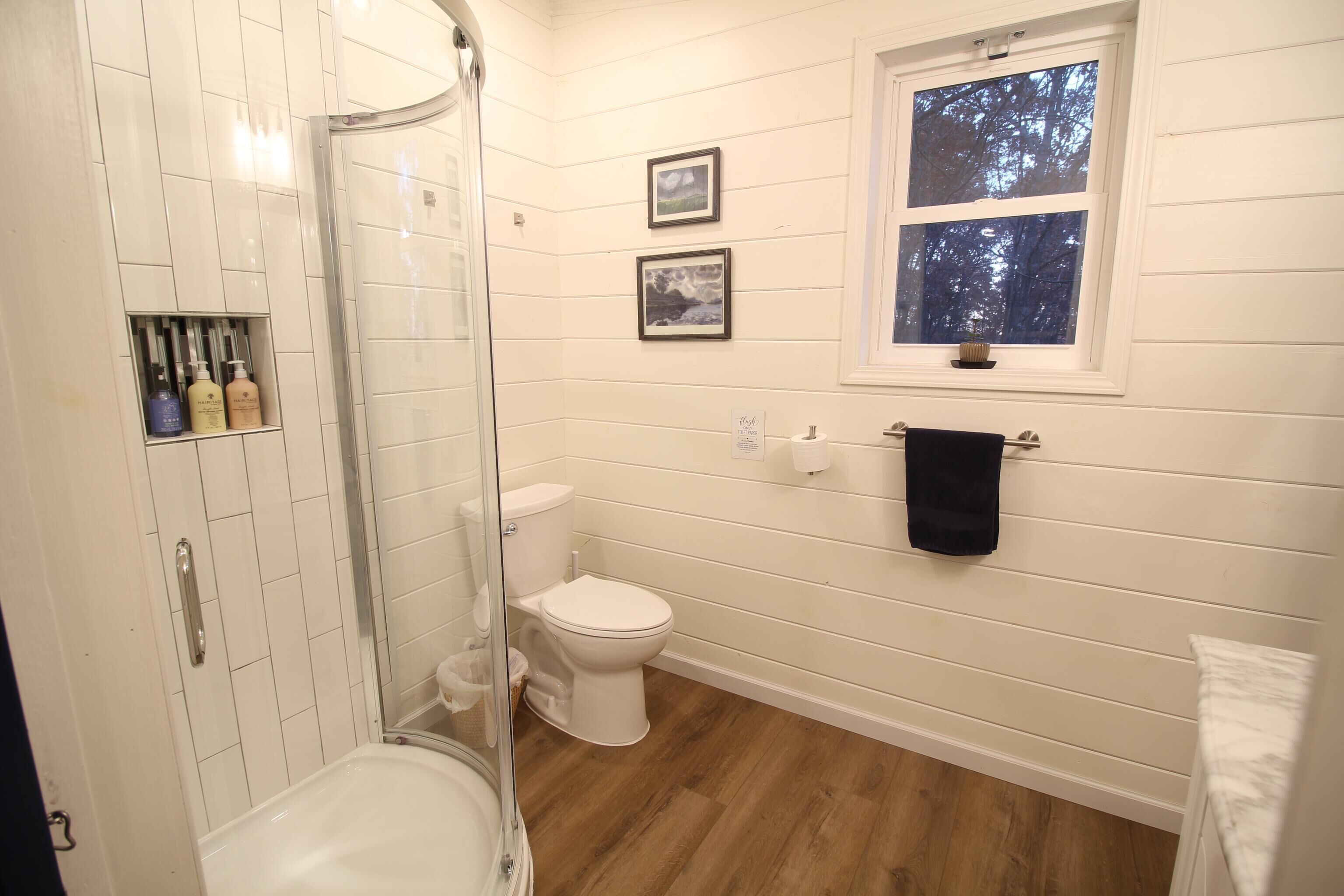 Une salle de bain avec douche, toilettes et une fenêtre donnant sur les arbres.