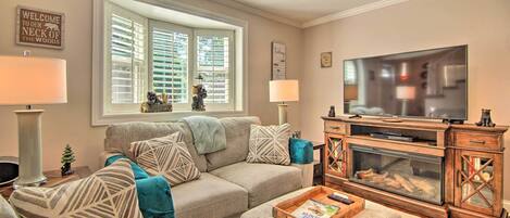 A living room with a beige sofa, a wooden entertainment center, and a large window with blinds.