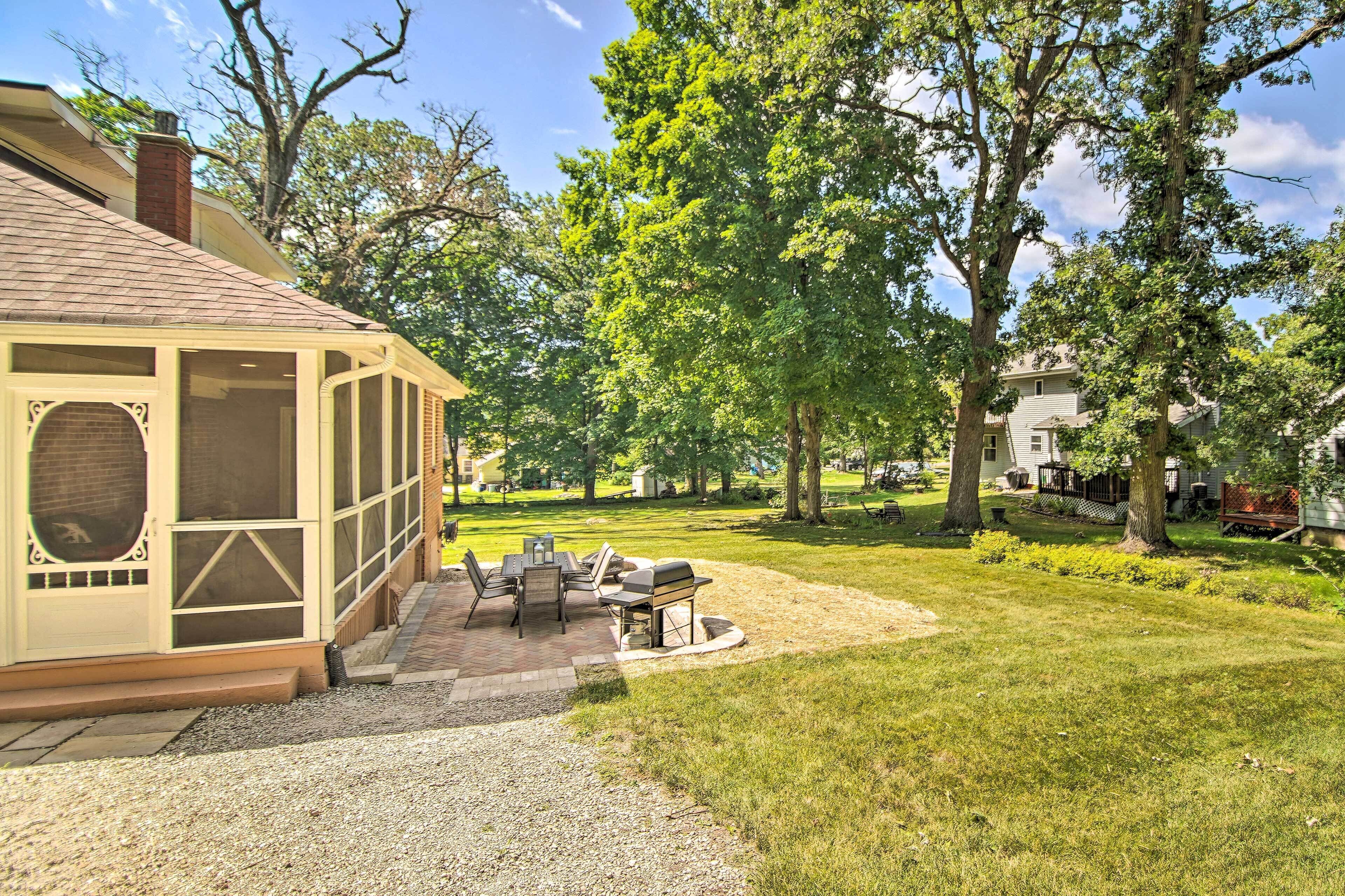 A covered patio with outdoor furniture, a grill, and a view of a grassy yard with trees.