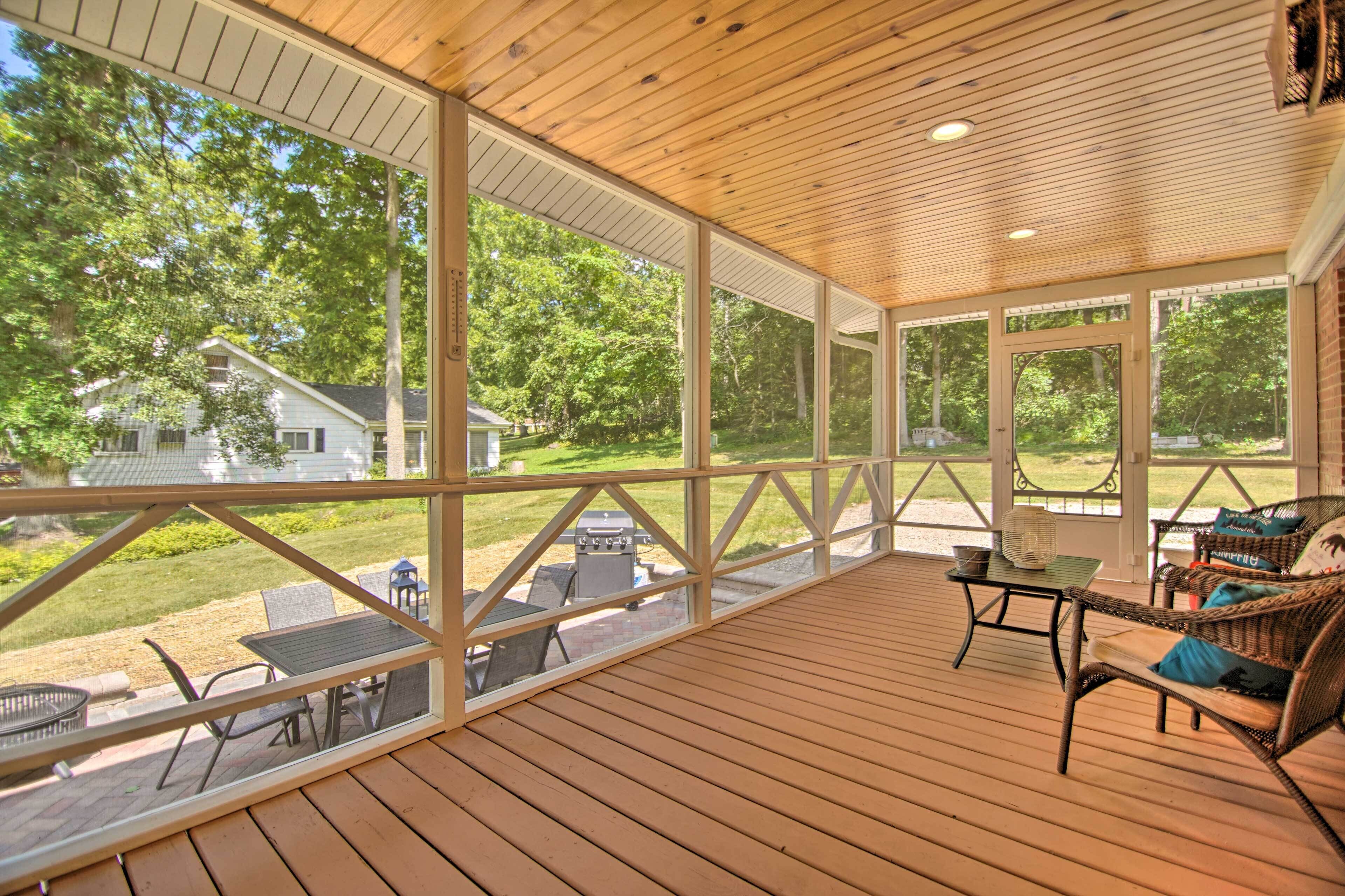 Eine überdachte Terrasse mit Holzboden, großen Fenstern und Gartenmöbeln.