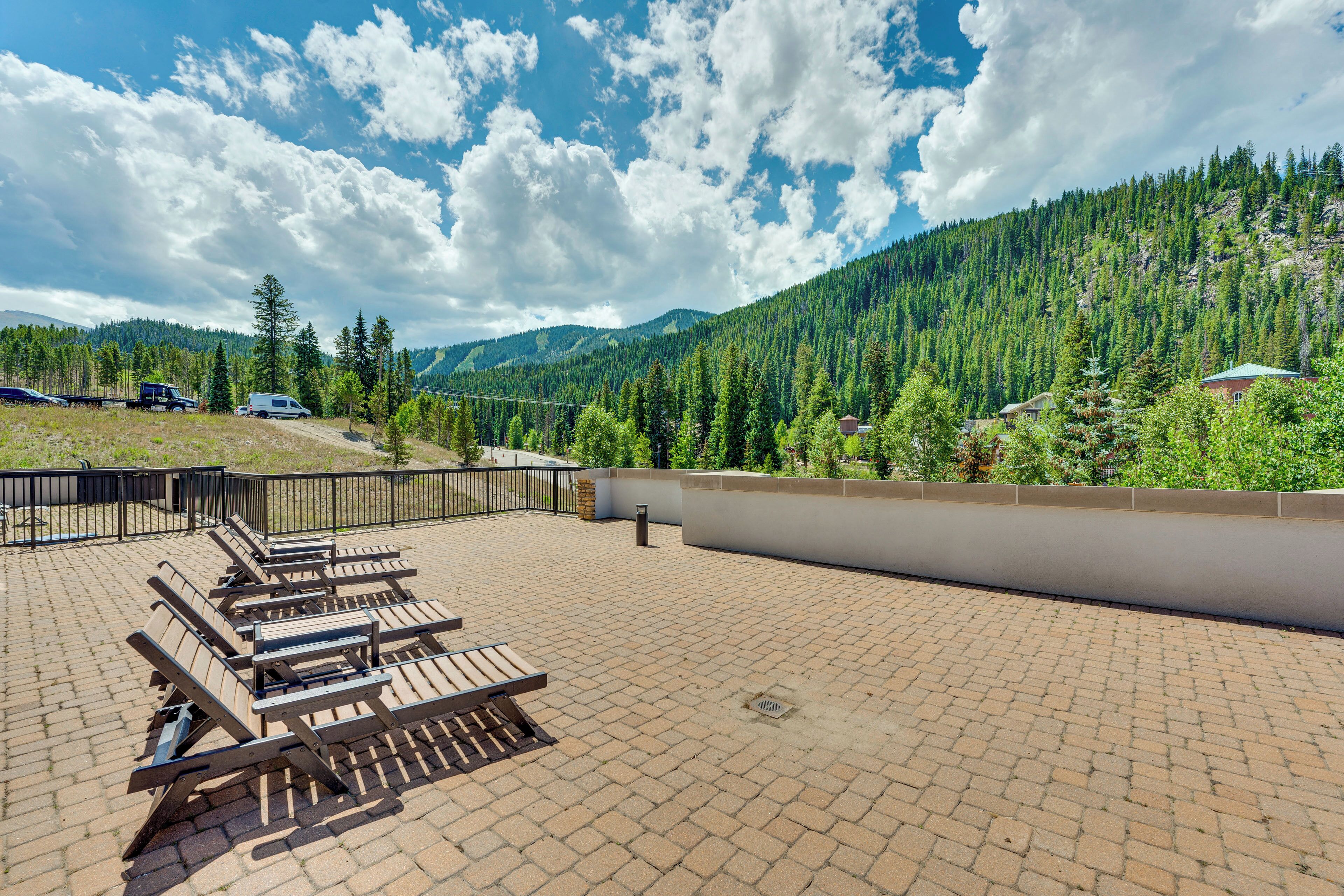 A rooftop patio with outdoor seating and a view of a forested mountain range.