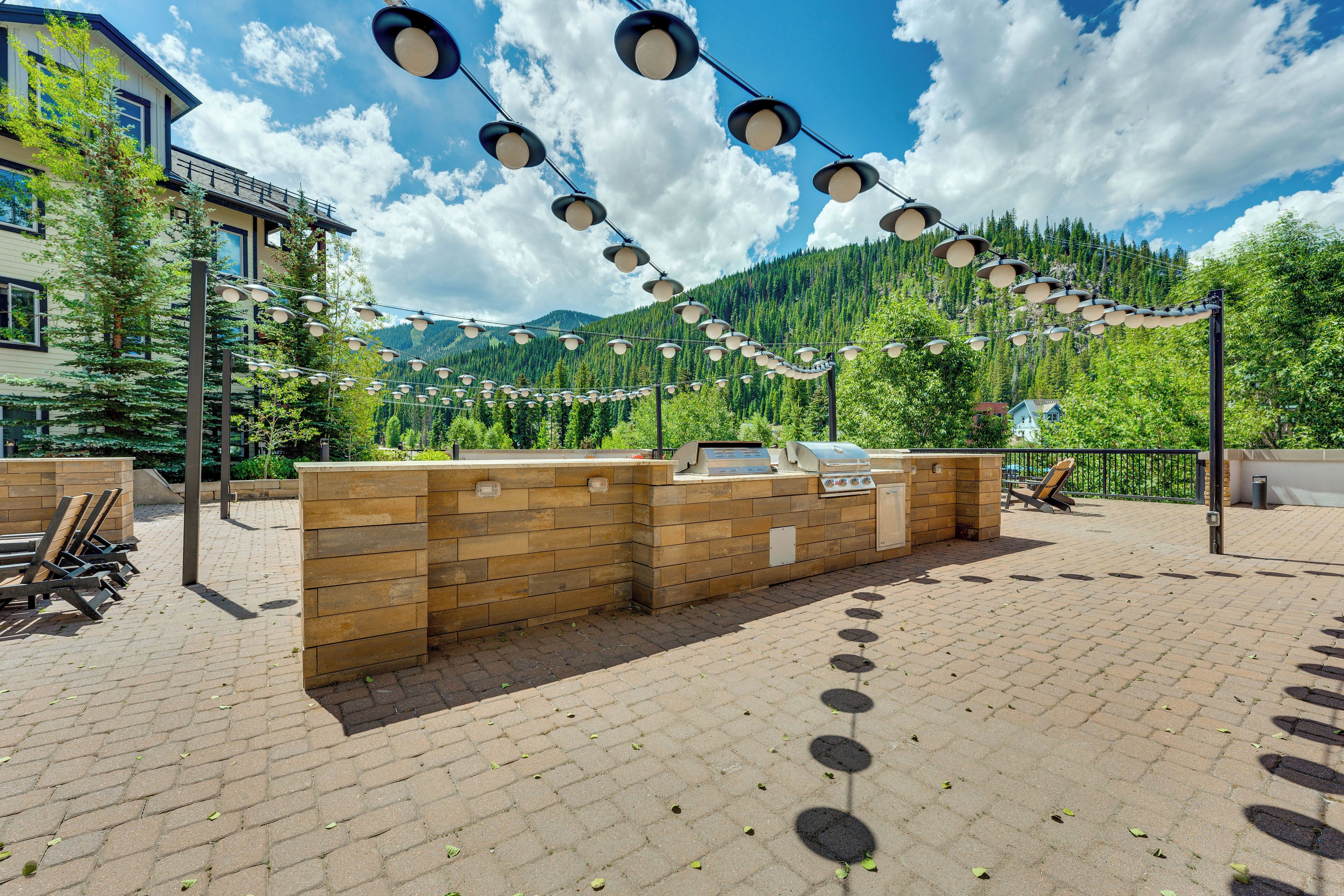 An outdoor patio area with a barbecue station, wooden seating, and a view of a mountain range.