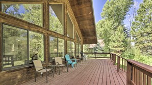 A wooden deck with large windows, outdoor seating, and a view of trees. - 'the River Home' Cabin w/ Yard: Near Wolf Creek! (Pagosa Springs)