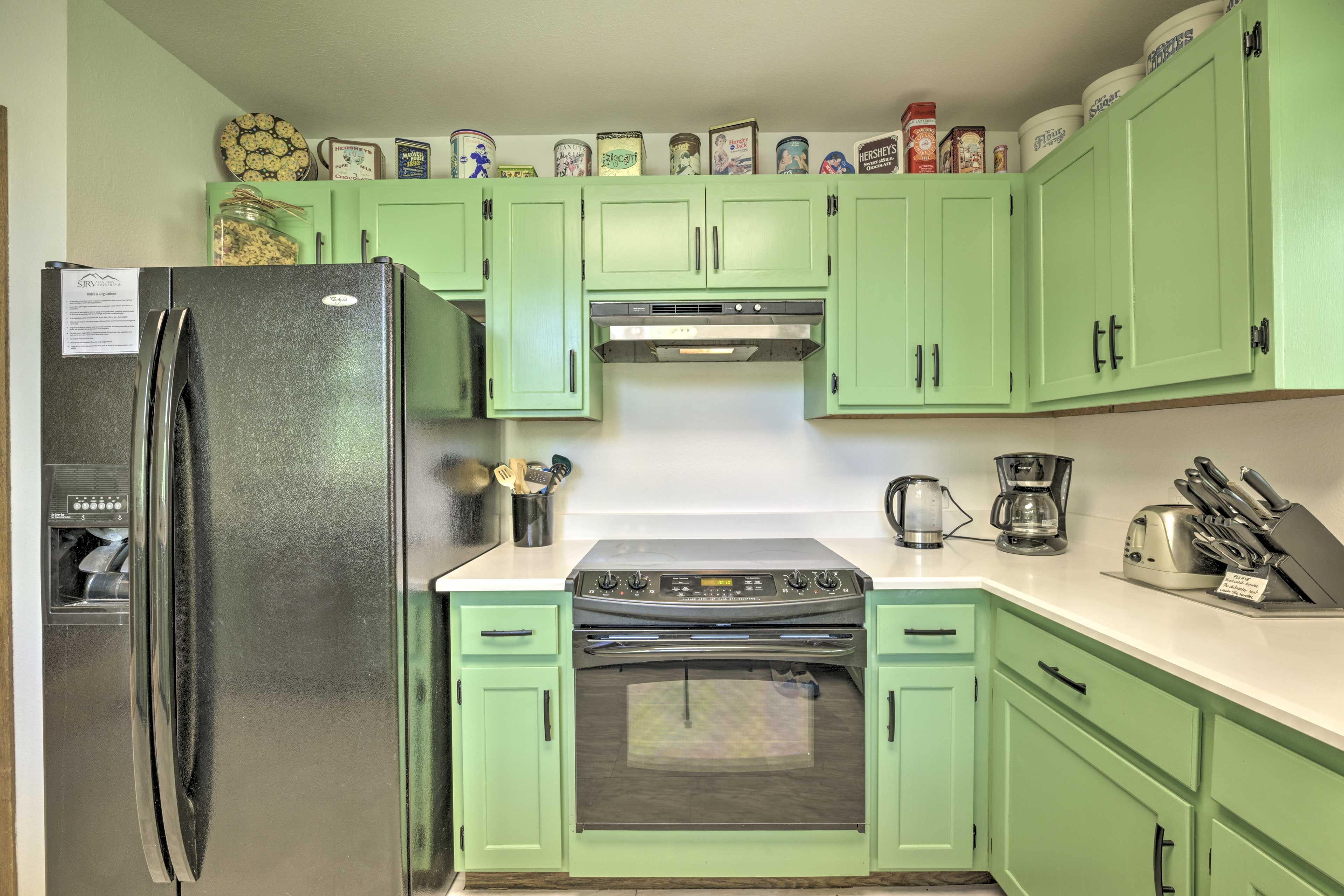 A kitchen with green cabinets, a stainless steel refrigerator, a stove, and various kitchen appliances.