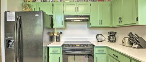 A kitchen with green cabinets, a stainless steel refrigerator, a stove, and various kitchen appliances.