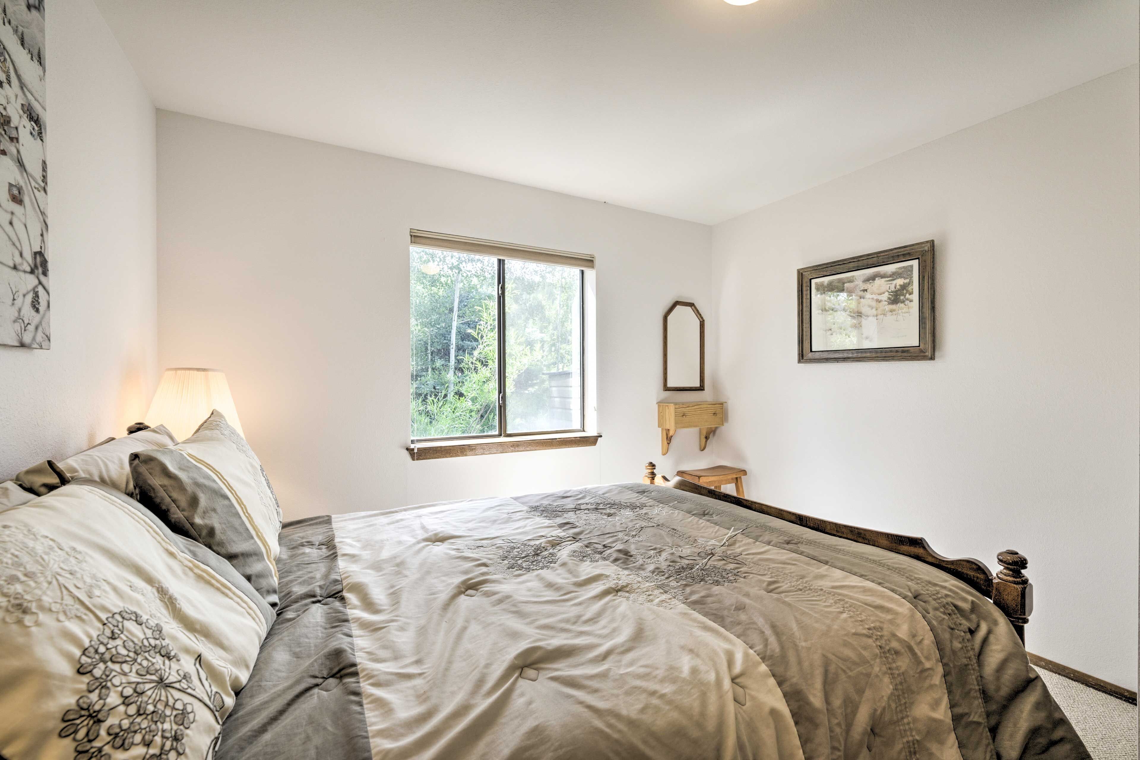 A bedroom with a bed, a window, a bedside table, and a wall-mounted shelf.