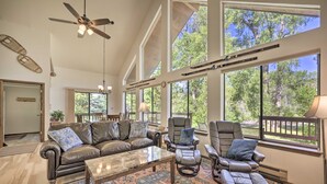 A spacious living room with leather furniture, large windows, and a ceiling fan. - 'the River Home' Cabin w/ Yard: Near Wolf Creek! (Pagosa Springs)