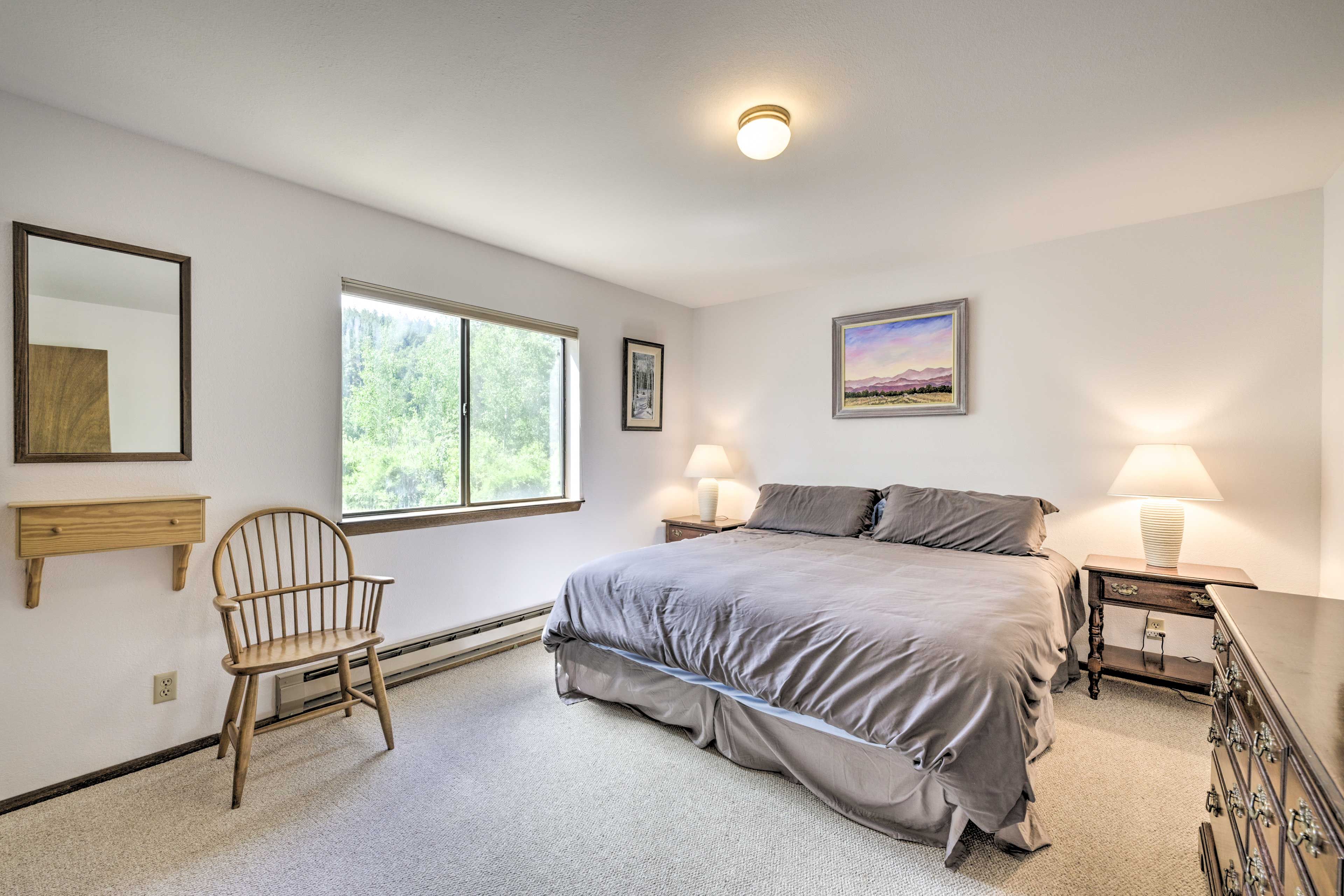 Une chambre à coucher avec un grand lit, une chaise, une table de chevet avec une lampe, une commode, une fenêtre et un tableau au mur.