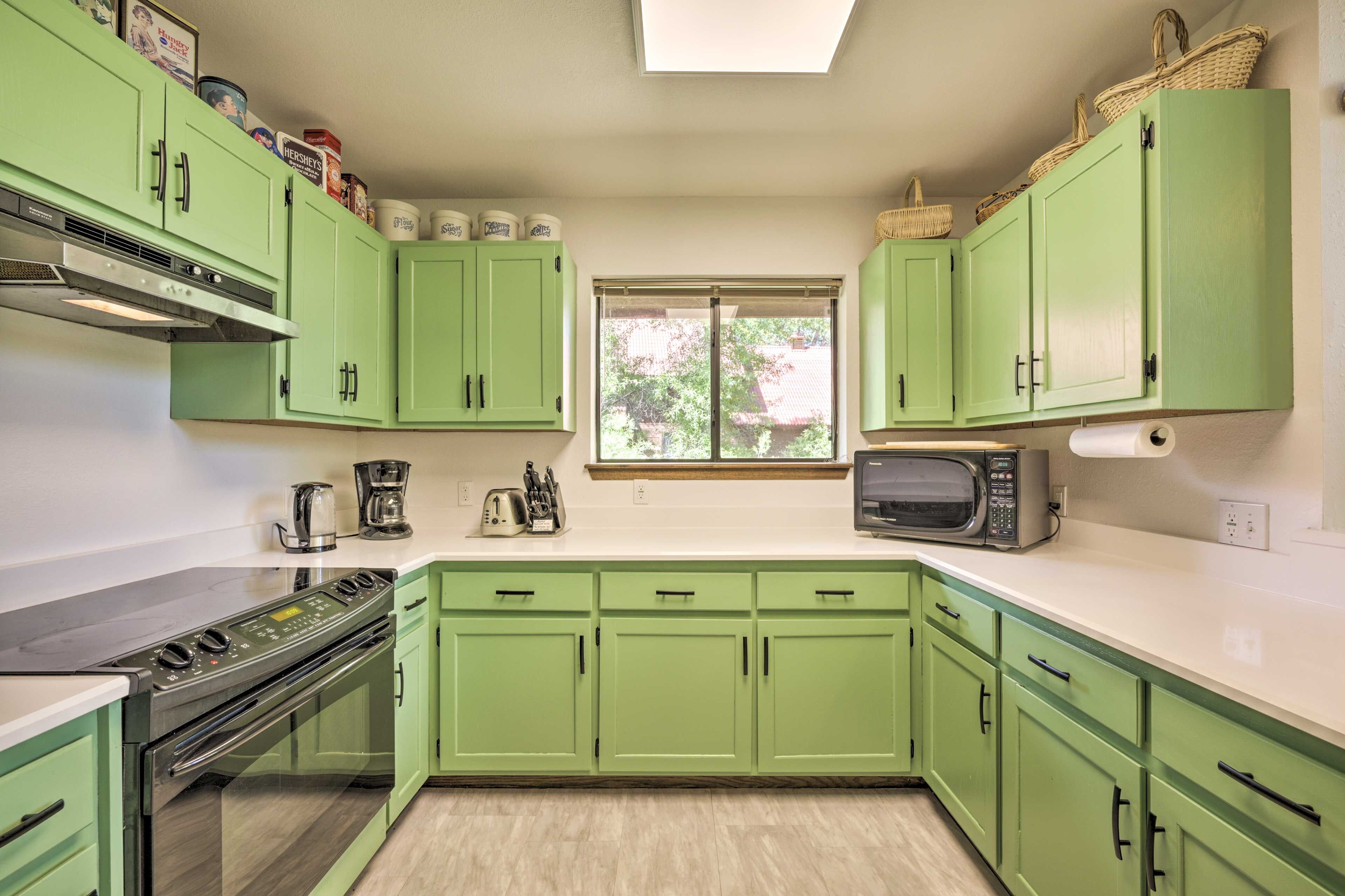 Une cuisine avec des meubles de rangement verts, une cuisinière, un four à micro-ondes et une fenêtre donnant sur des arbres.