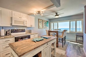 A kitchen with white cabinets, a wooden countertop, a stove, and a dining area with a table and chairs. - PCB Beachfront 'coastal Abode' at Pinnacle Port! (Panama City Beach)